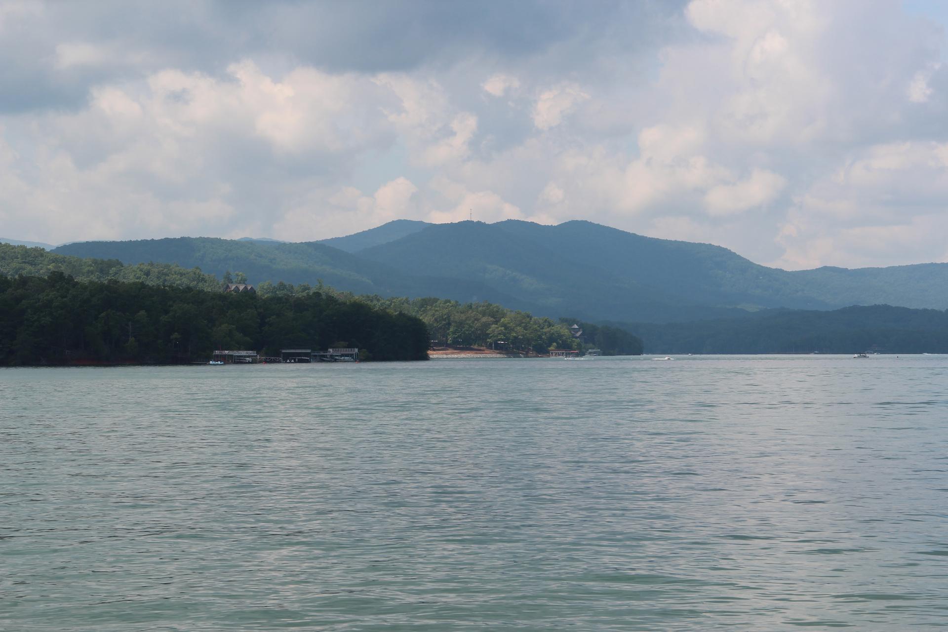 A wide lake with distant forested shores and mountains under a cloudy sky.
