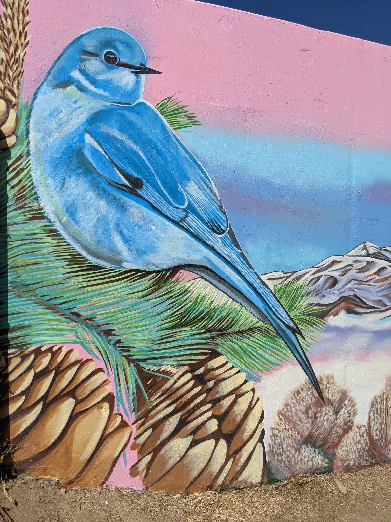 Vibrant mural of a blue bird perched on pine branches with mountains.