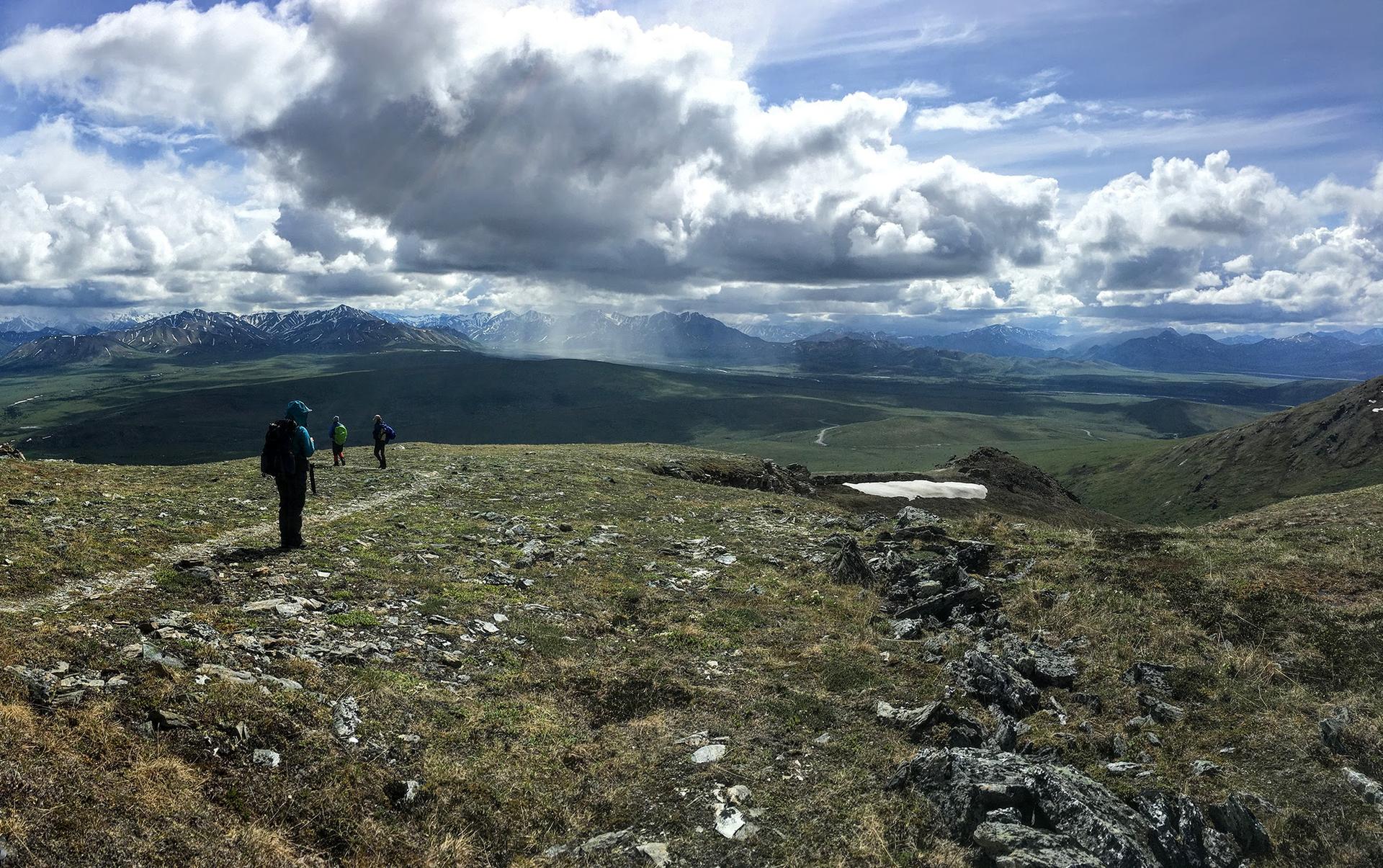 Three hikers on a mountain ridge under dramatic cloudy skies.