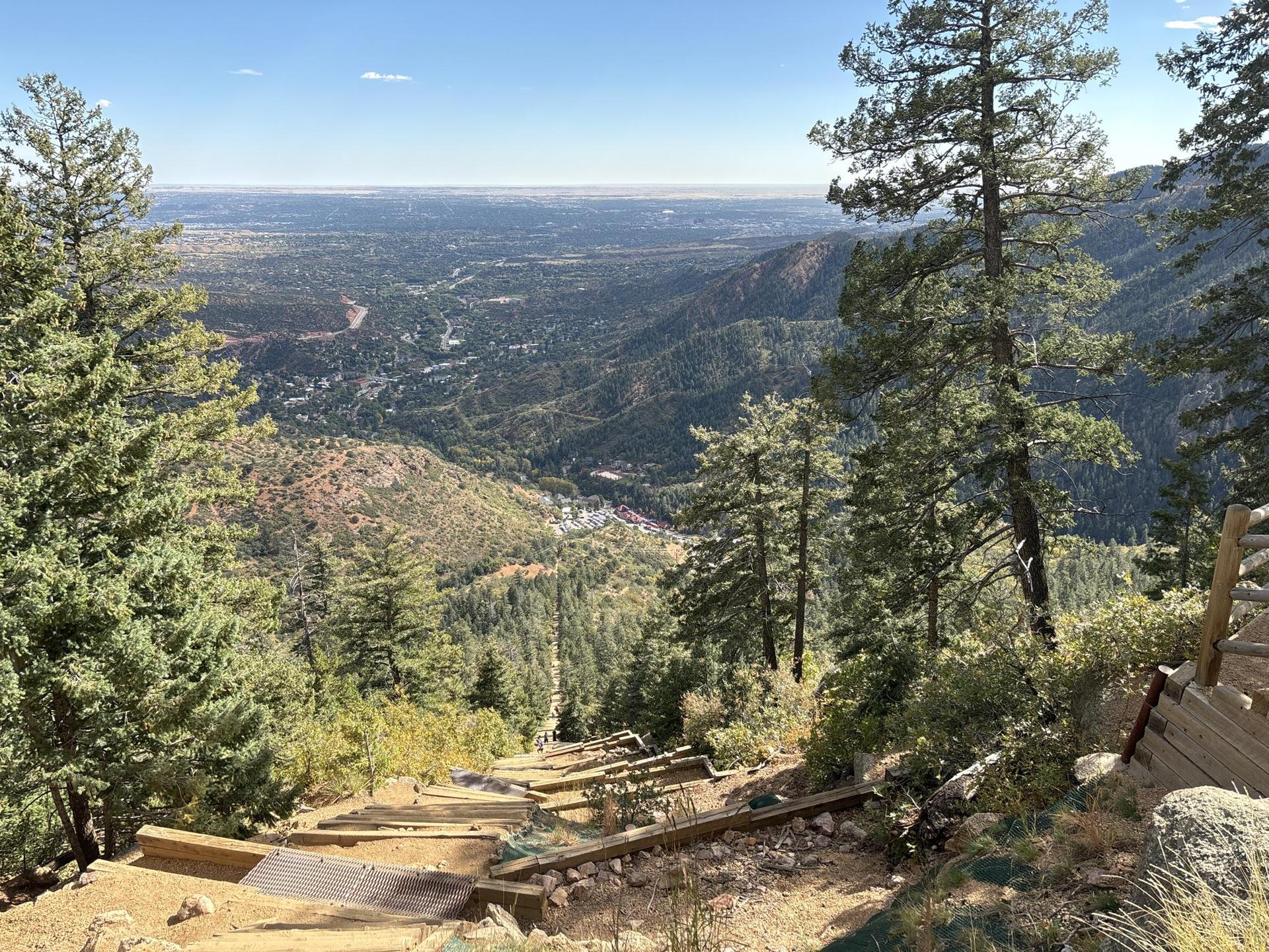 Steep wooden stairs descending a mountain, overlooking a green valley. Sunny day.