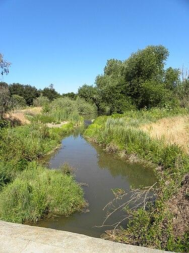 A winding river with green banks under a bright, clear blue sky.