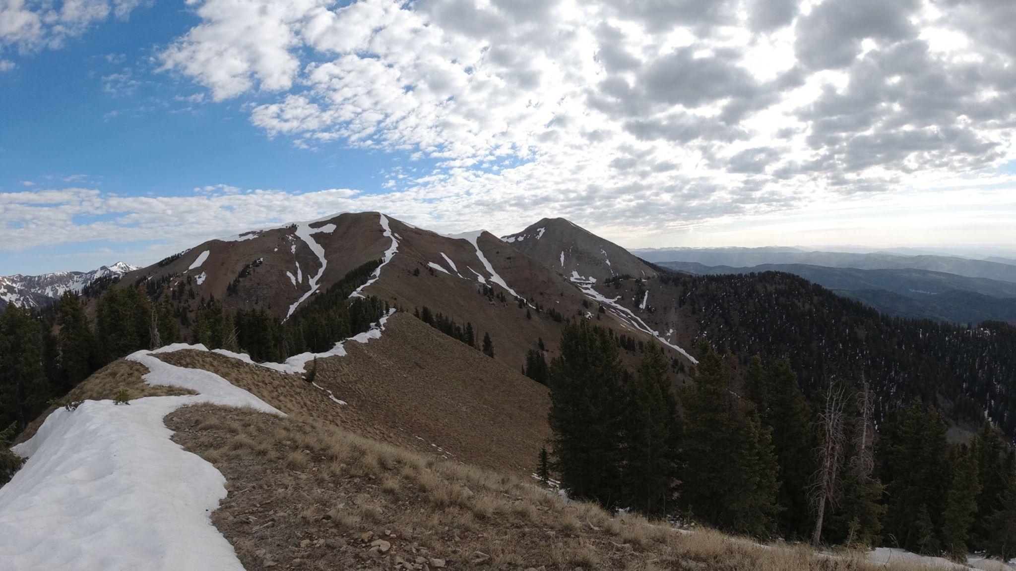 Panoramic view of a mountain ridge with snow patches under a partly cloudy sky.