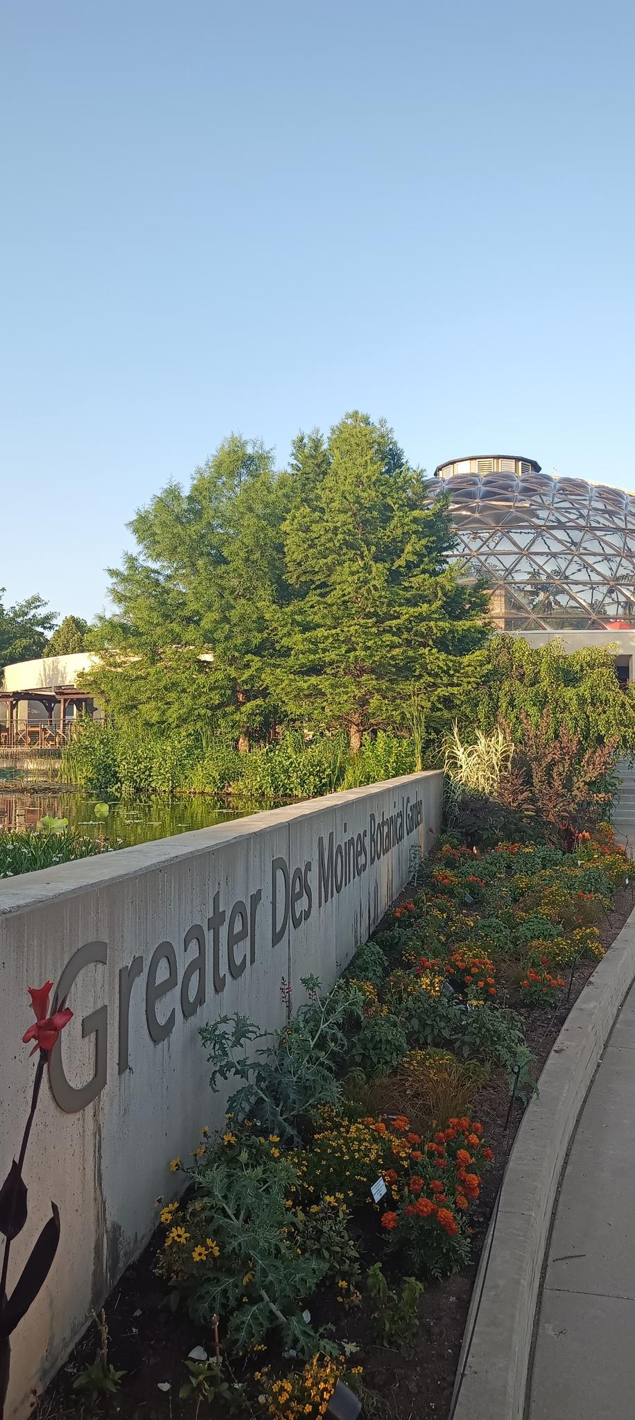 Concrete wall with garden bed, glass dome building, and trees under clear sky.