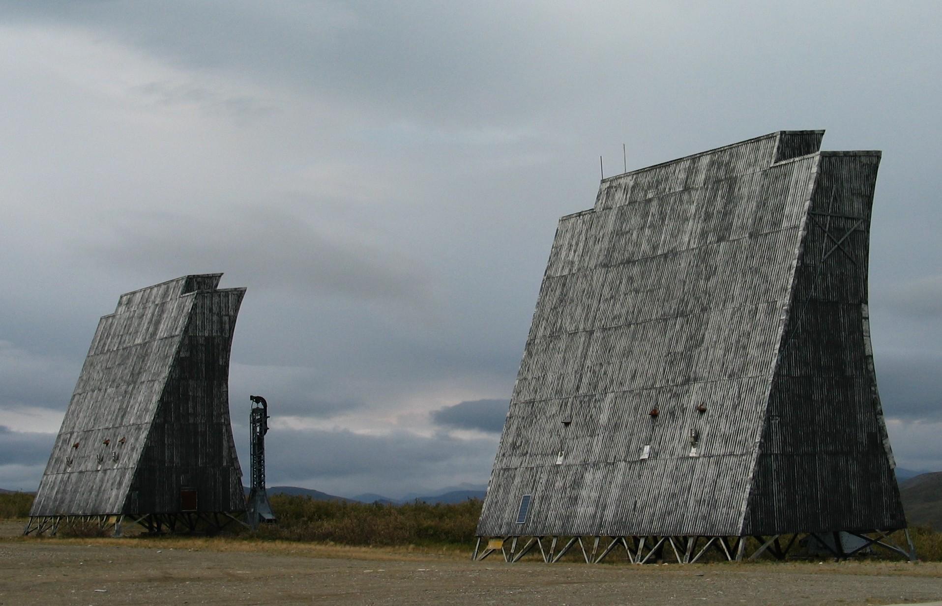 Two large, weathered wooden structures stand under a cloudy, overcast sky.