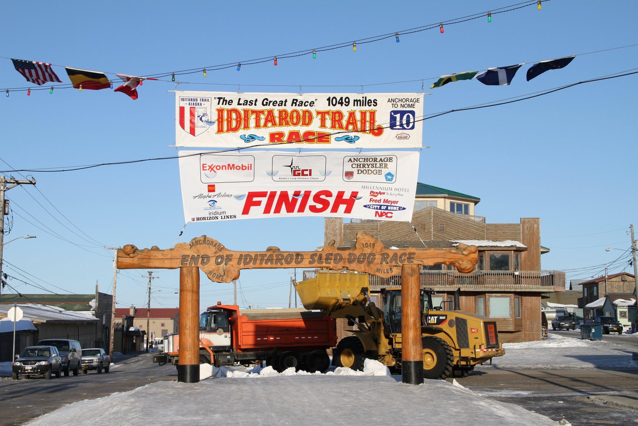 Large finish line banner over a snowy street with heavy equipment under bright sun.