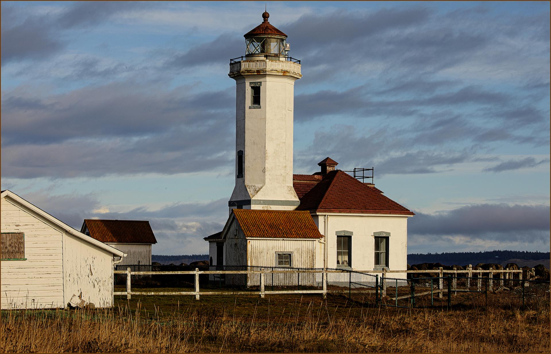A tall white lighthouse with a red roof under a cloudy sky.