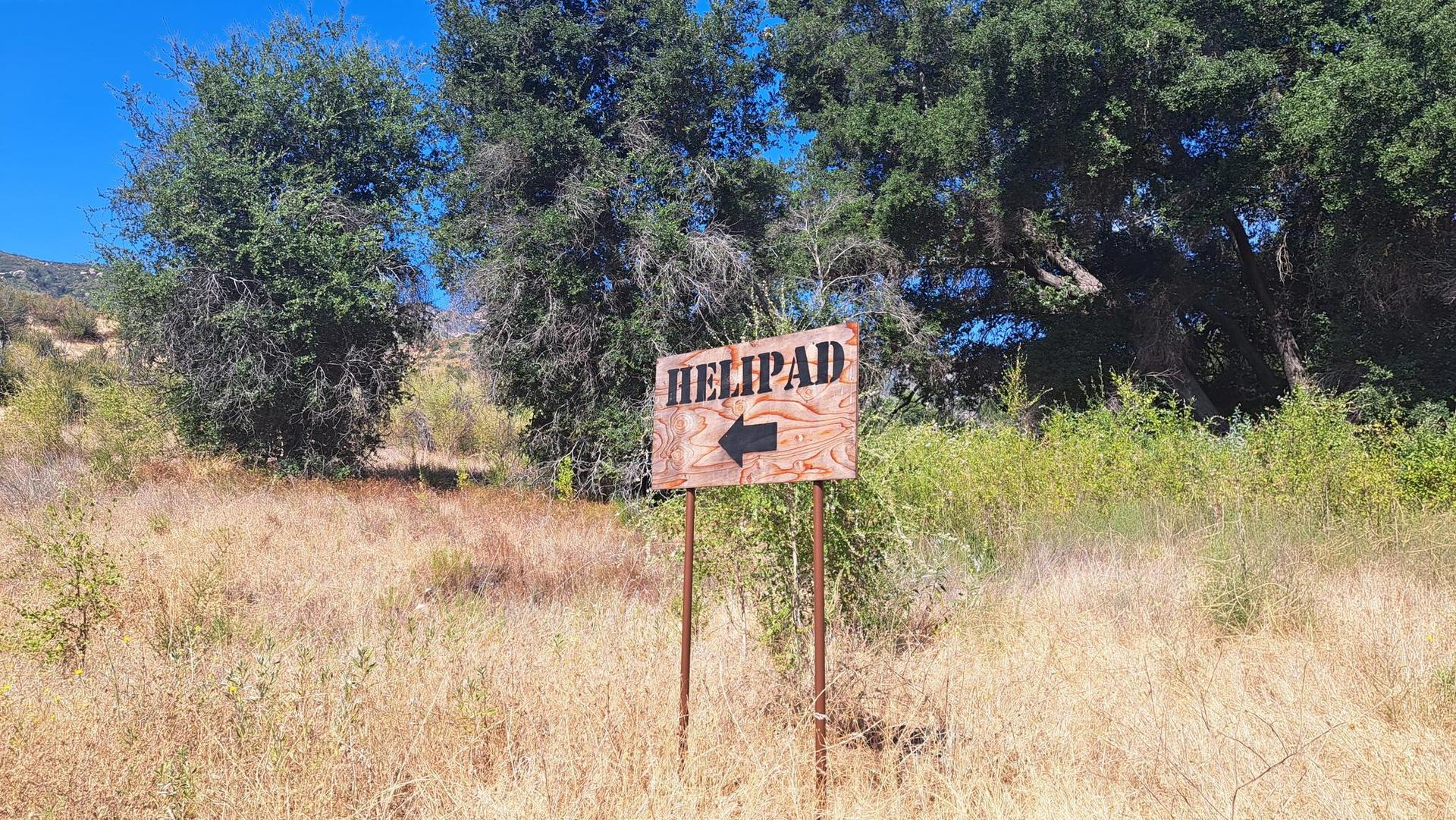 Wooden "HELIPAD" sign with an arrow in dry grass, bright daylight.