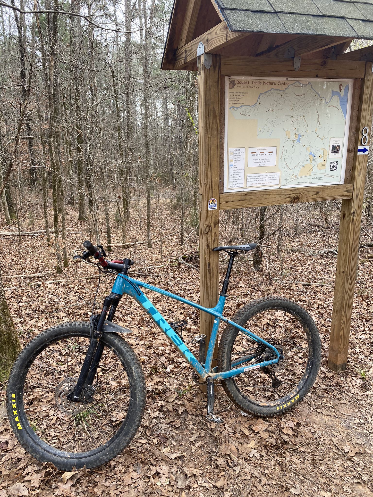 Blue mountain bike parked beside a wooden trail map in a bare forest. - Lakeside Pavilion – Dauset Trails Connector loop from Dauset Trails Biking Trailhead