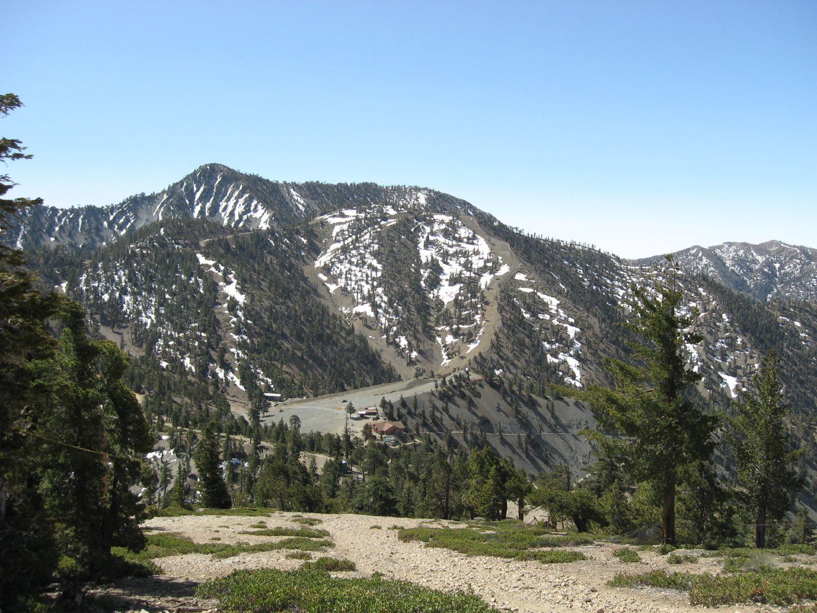 Snow-dusted mountain with evergreen trees and buildings in a valley below.