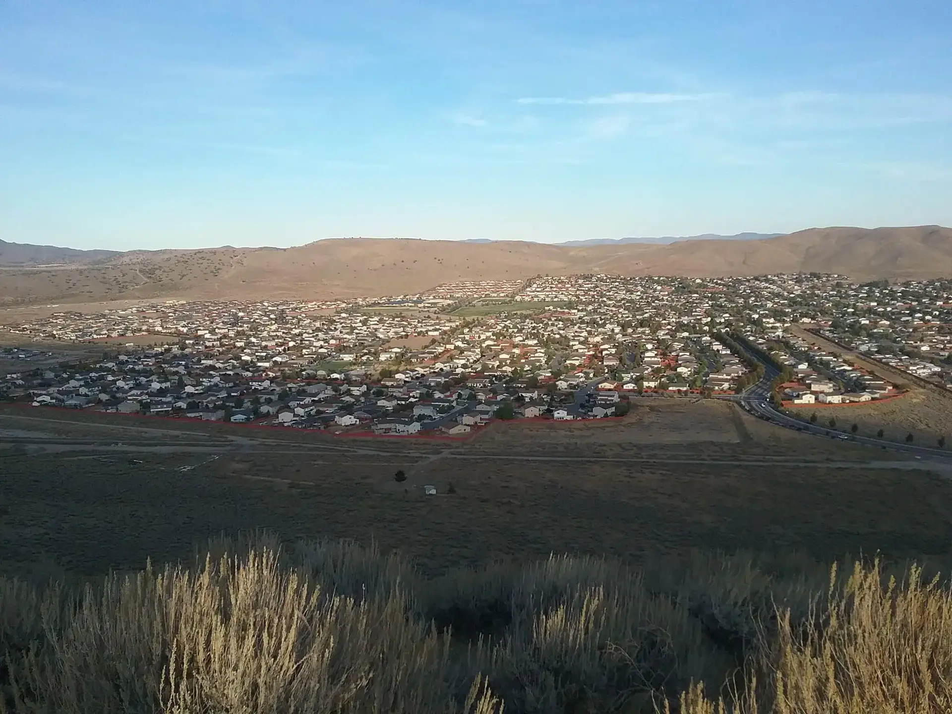 Expansive residential area in a valley, surrounded by hills under bright sky.