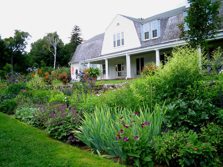 Large white house with porch overlooks a vibrant, multi-tiered garden.