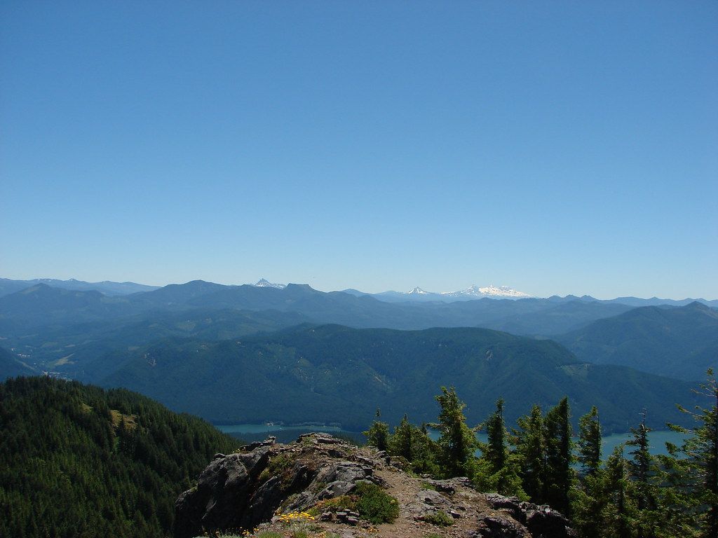 Sunny mountain vista with forested slopes, a lake, and distant snow-capped peaks. - Tumble Ridge Trail #3380