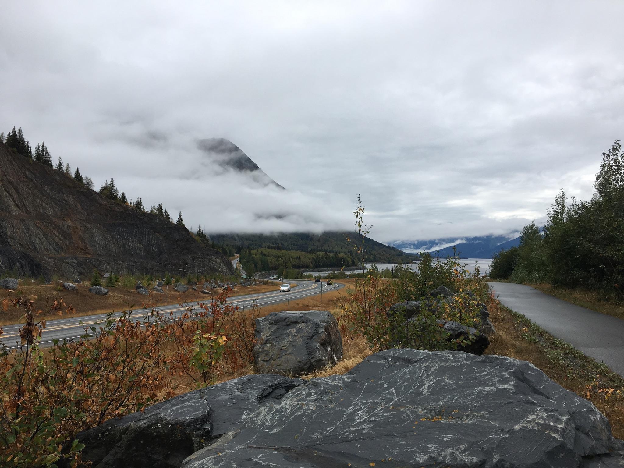 Highway winding through mountains under a cloudy sky, with cars.