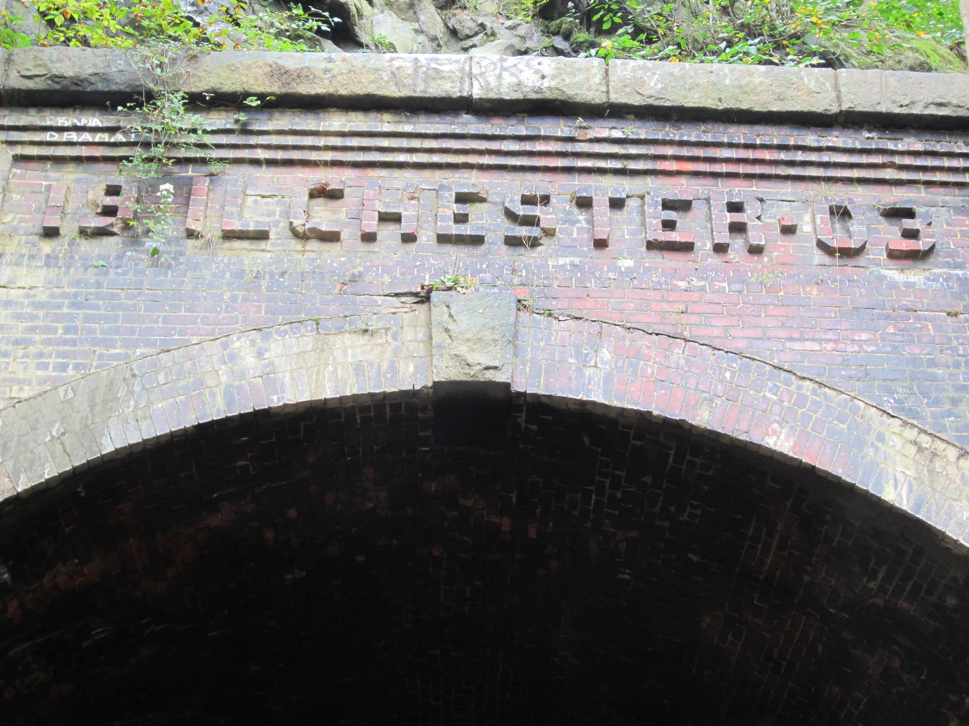 Brick archway entrance to a dark tunnel with text carved above.