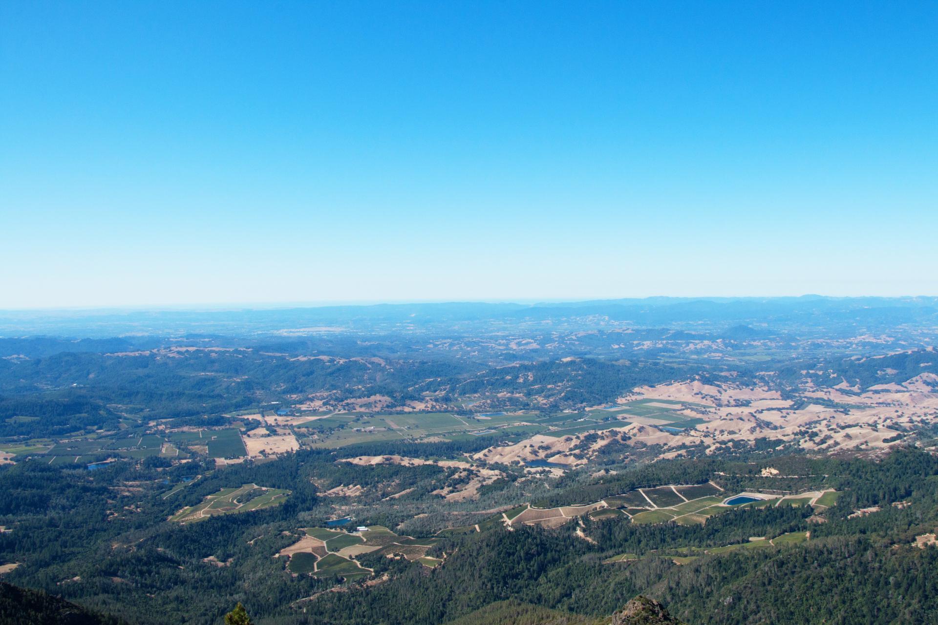 Vast landscape with forested hills and cultivated fields under bright daylight.
