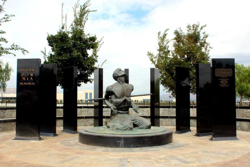 Bronze statue of a kneeling figure surrounded by black memorial plaques under an overcast sky.