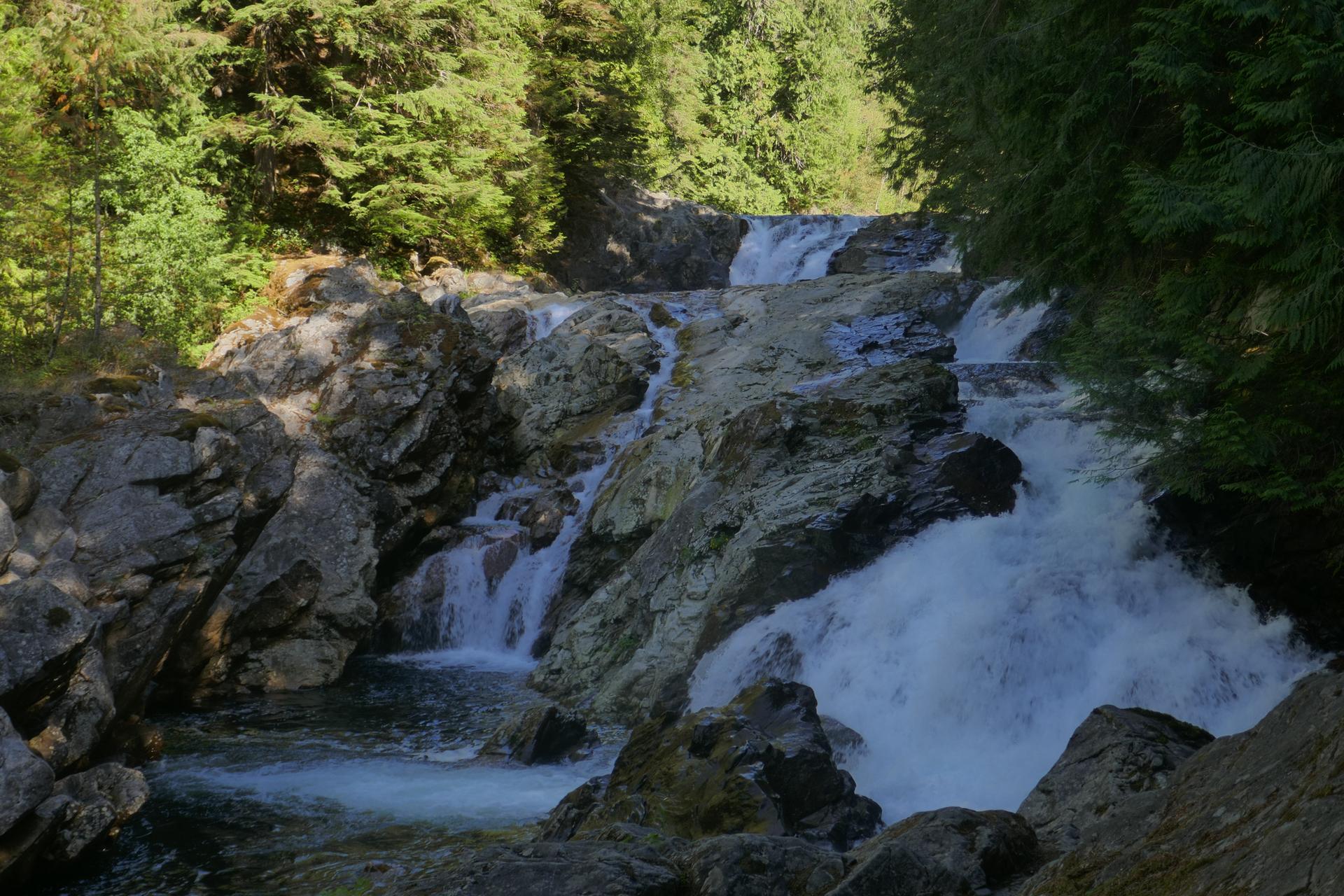 Multi-tiered waterfall cascades over dark rocks in a lush green forest.