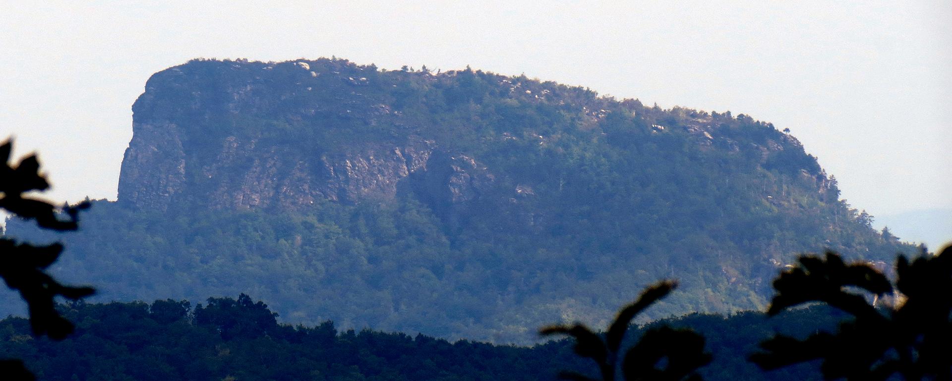 Hazy view of a dark, flat-topped mountain covered in trees.