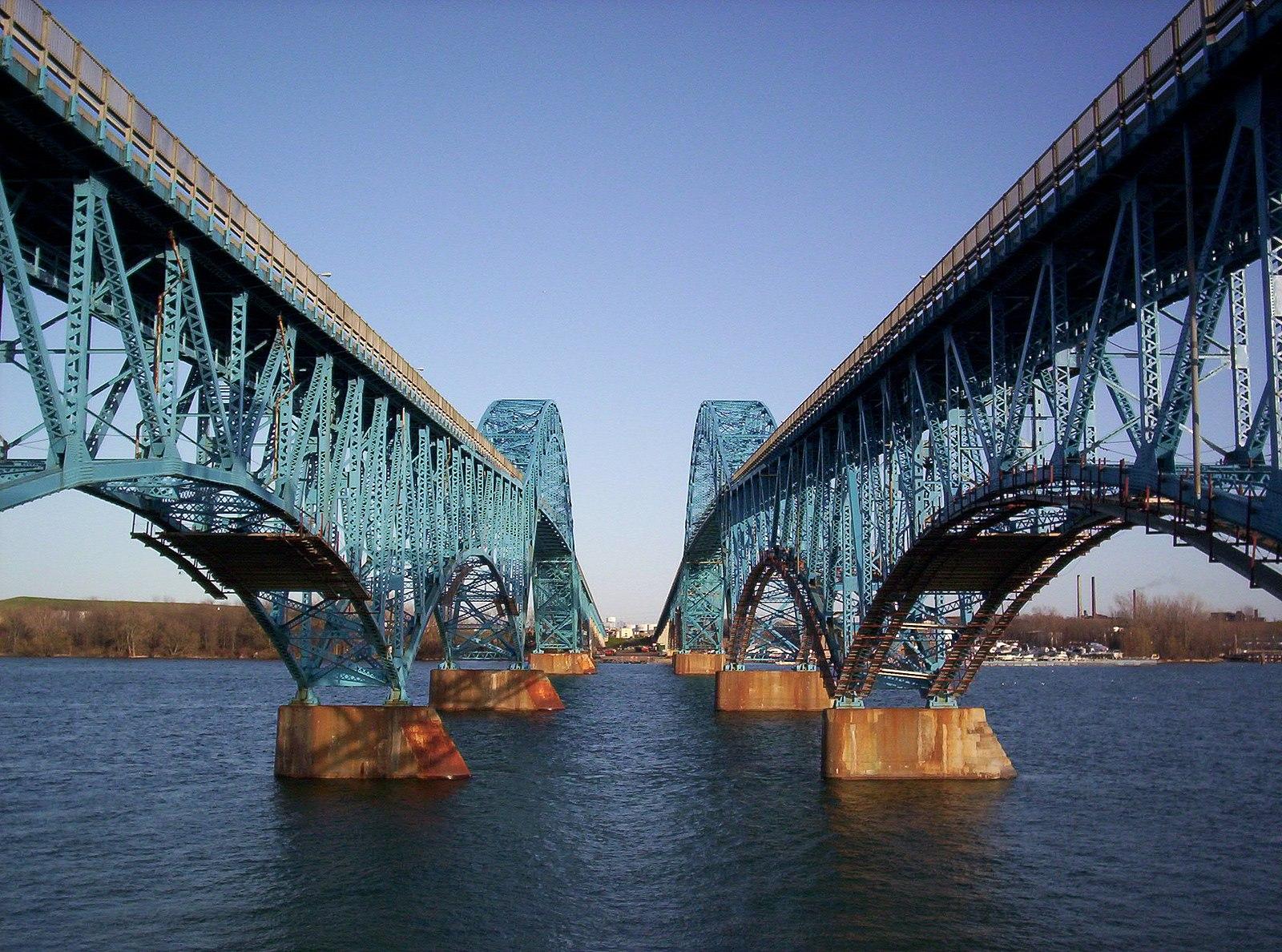 Two massive blue metal bridges span across wide, calm blue water.