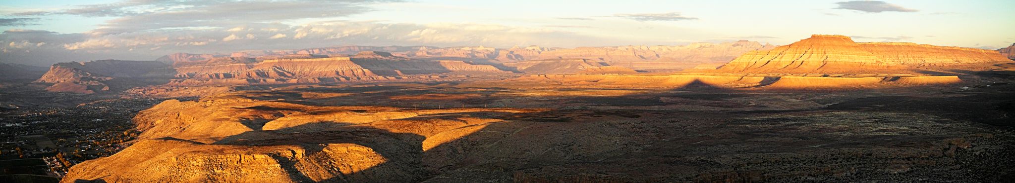 Golden hour light illuminates a vast desert landscape with mesas and long shadows. - Honeymoon Trail