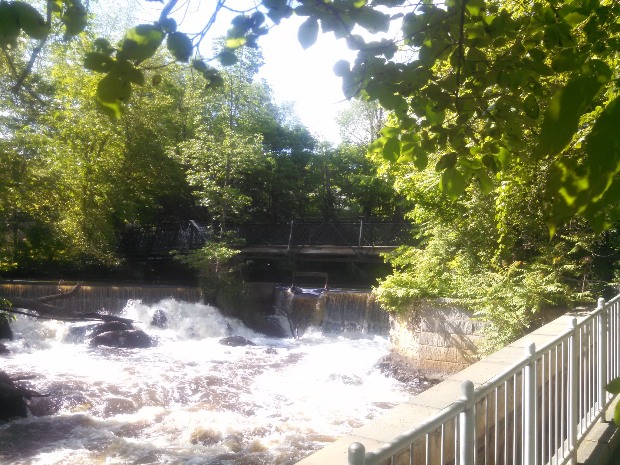 Rushing river with small waterfalls, bordered by a white railing and green trees. - Echo Bridge – Sudbury Aqueduct Path loop from Boulder Brook Reservation