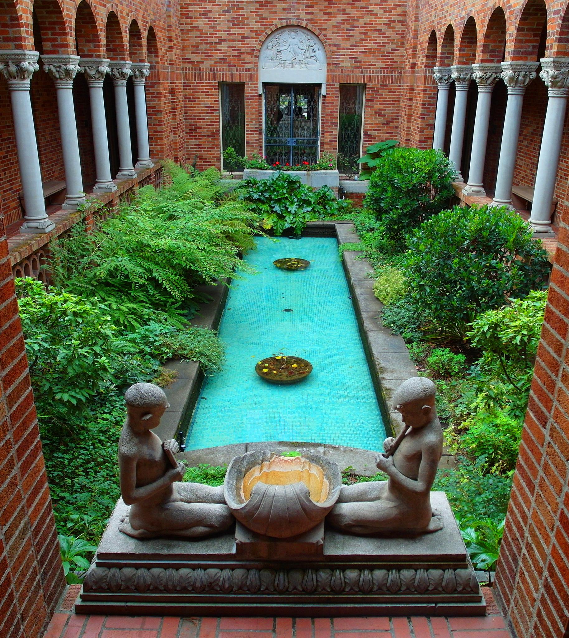 A serene courtyard with a turquoise pool, lush plants, brick arches, and statues.