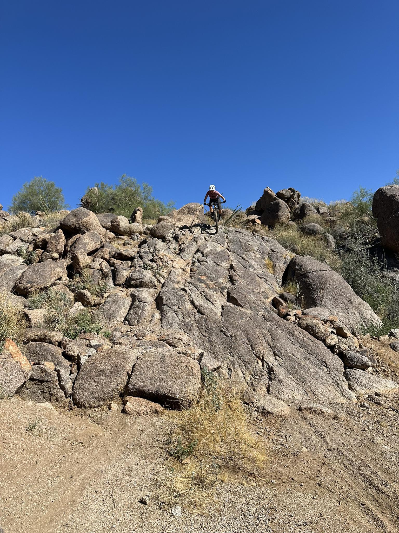 Mountain biker descending a steep, rocky desert slope under a clear sky.