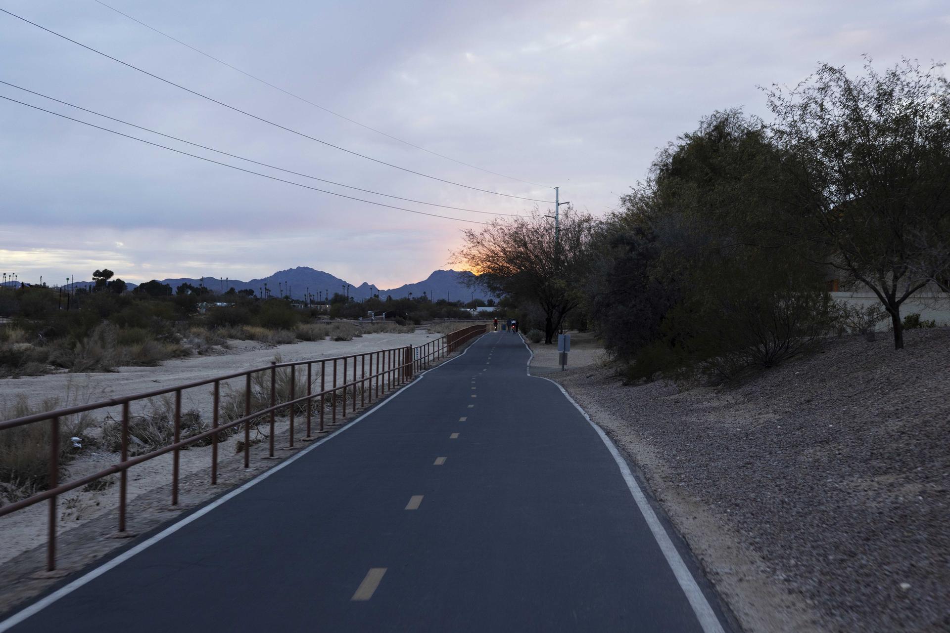 Paved path at dusk with mountains, trees, and a person walking.