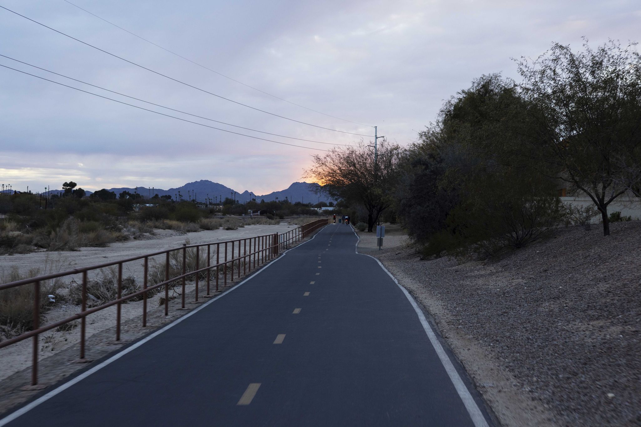Paved path at dusk with mountains, trees, and a person walking. - Rillito River Path Loop