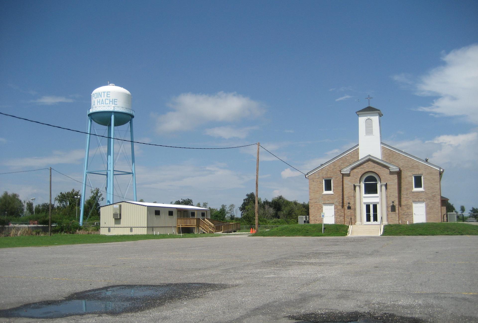 A tall water tower stands beside a brick church under a bright blue sky.
