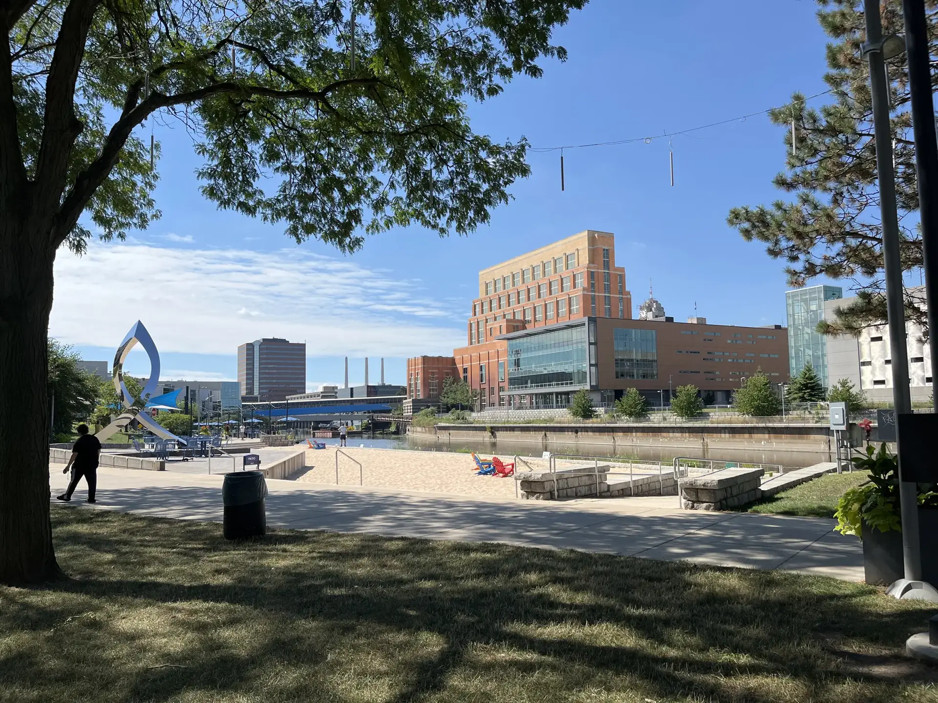 Sunny urban waterfront with a sandy beach, buildings, and a few people.