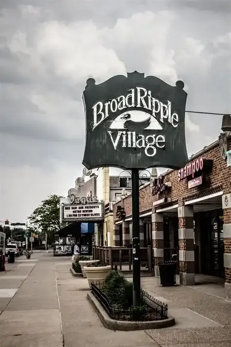 A large dark sign on a cloudy day in front of brick storefronts. - Indiana State Capitol Building – Broad Ripple Village loop from Indianapolis Union Station