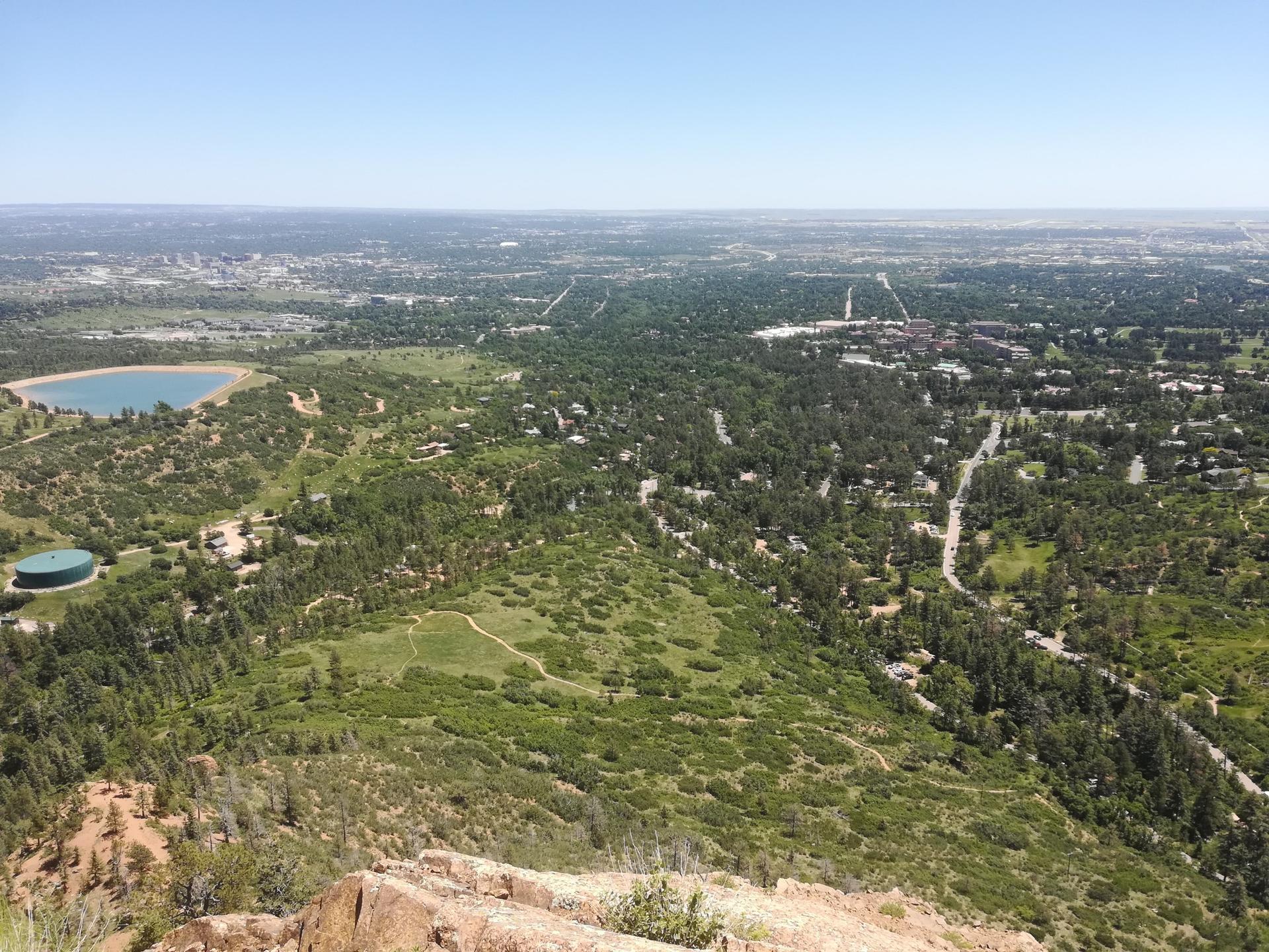 Wide aerial view of green hills, a blue reservoir, and a distant city.