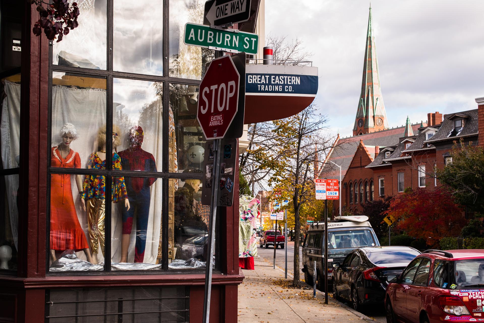 Storefront window with mannequins, street signs, and a distant church spire.