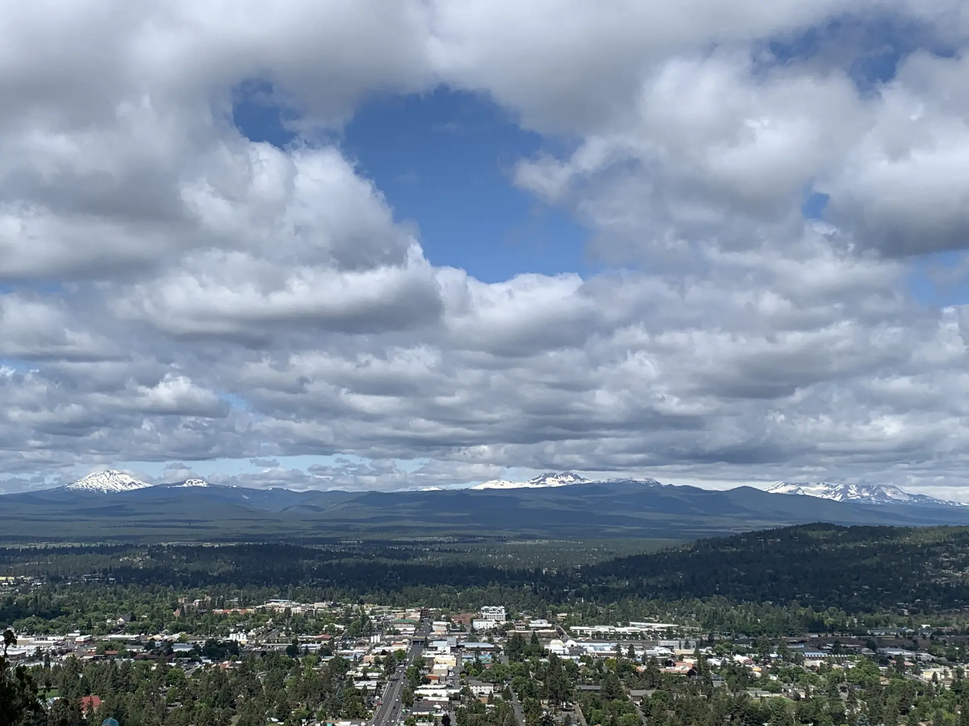 Panoramic view of a town with distant snow-capped mountains under cloudy skies.