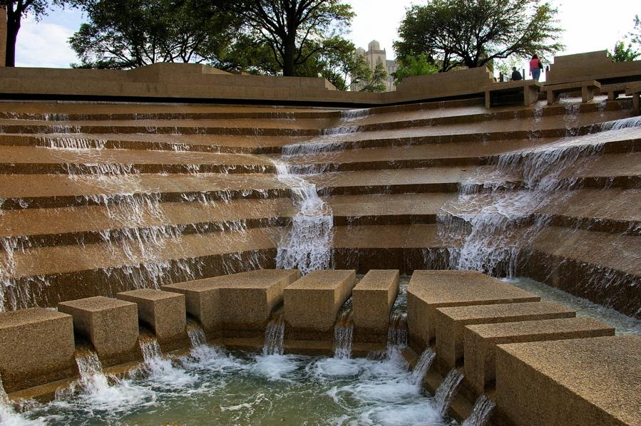 Terraced concrete water feature with cascading water under bright daylight.