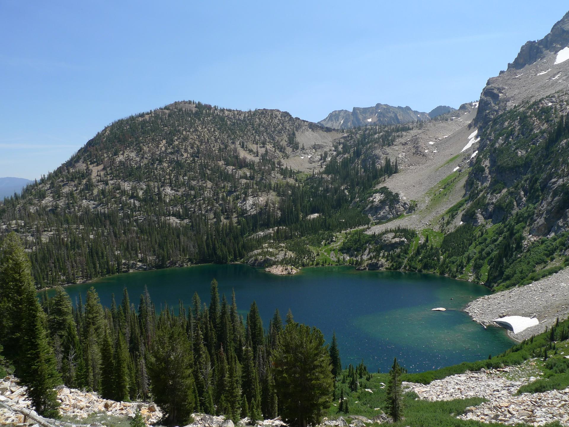 A deep blue alpine lake surrounded by forested and rocky mountains.