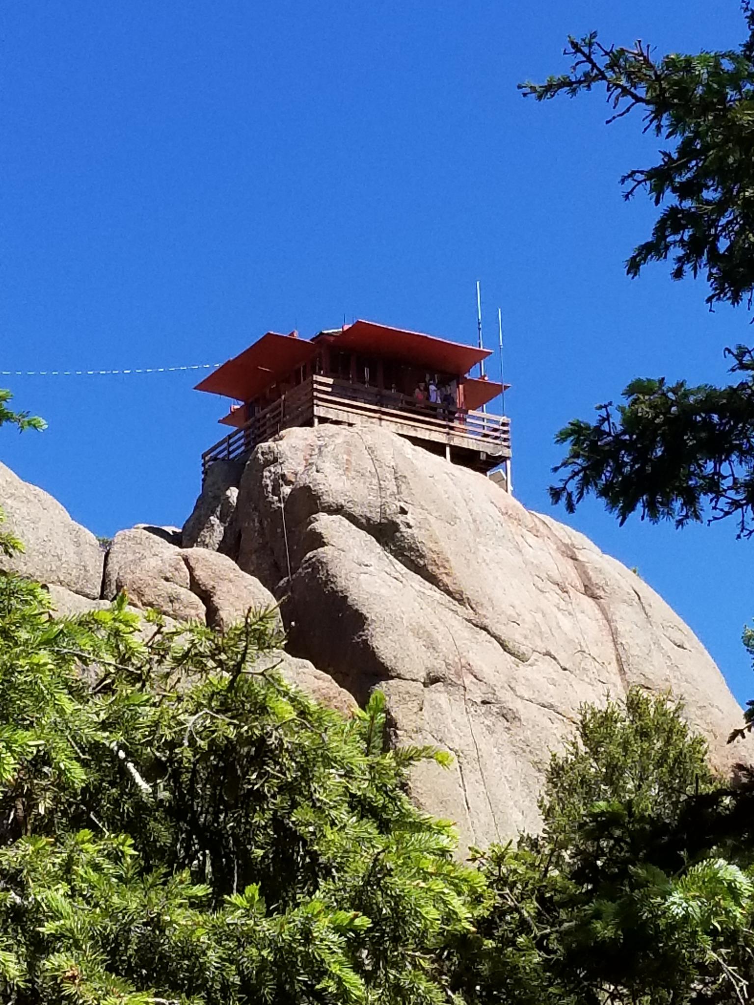 Fire lookout tower on a rocky peak under a clear blue sky.