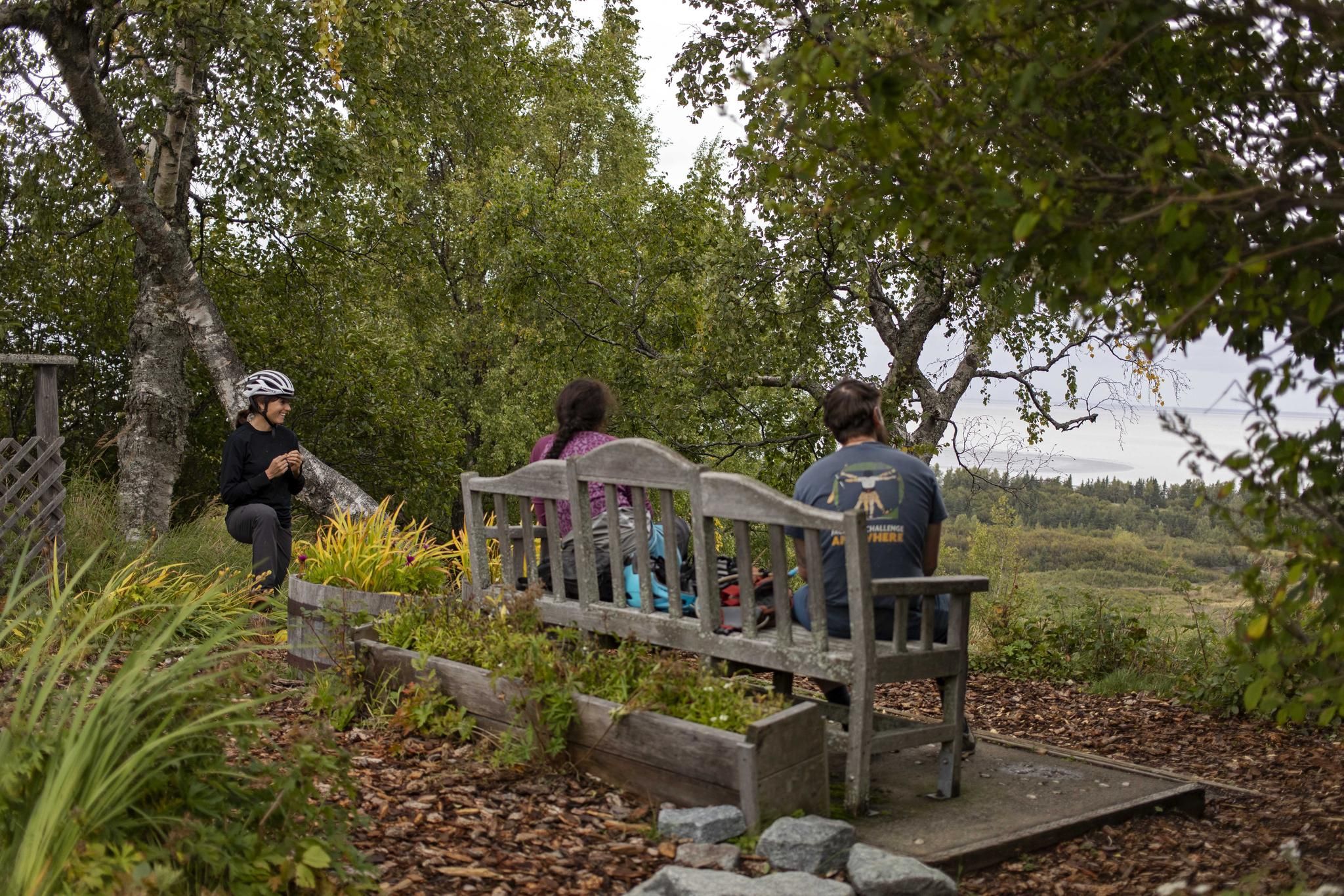 Three people relaxing outdoors, two on a bench, surrounded by green trees. - Margaux's and Mize Loop