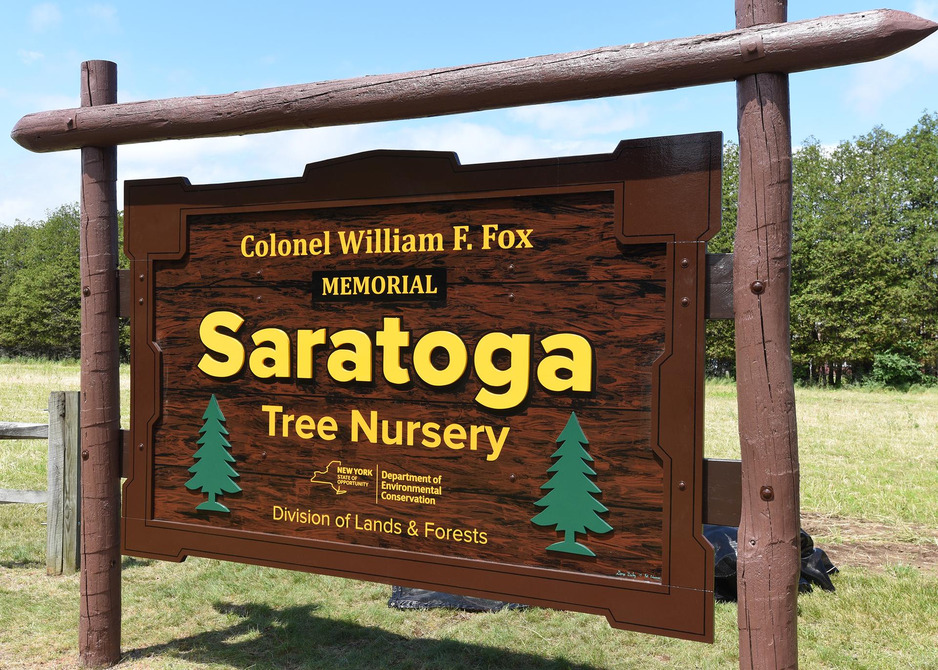 A brown wooden sign with text and tree graphics in a bright, grassy landscape.