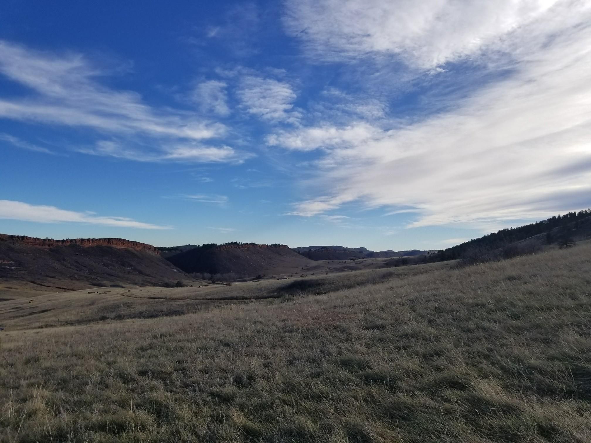 Wide view of a vast, dry grassy valley under a dramatic blue sky. - Howard and Westridge Loop Trail