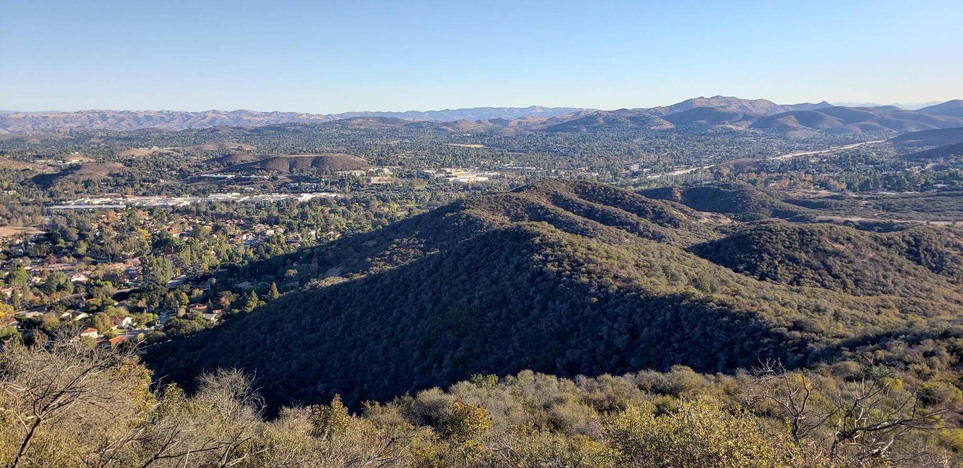 Vast landscape of sun-dappled hills and distant town under a bright blue sky.