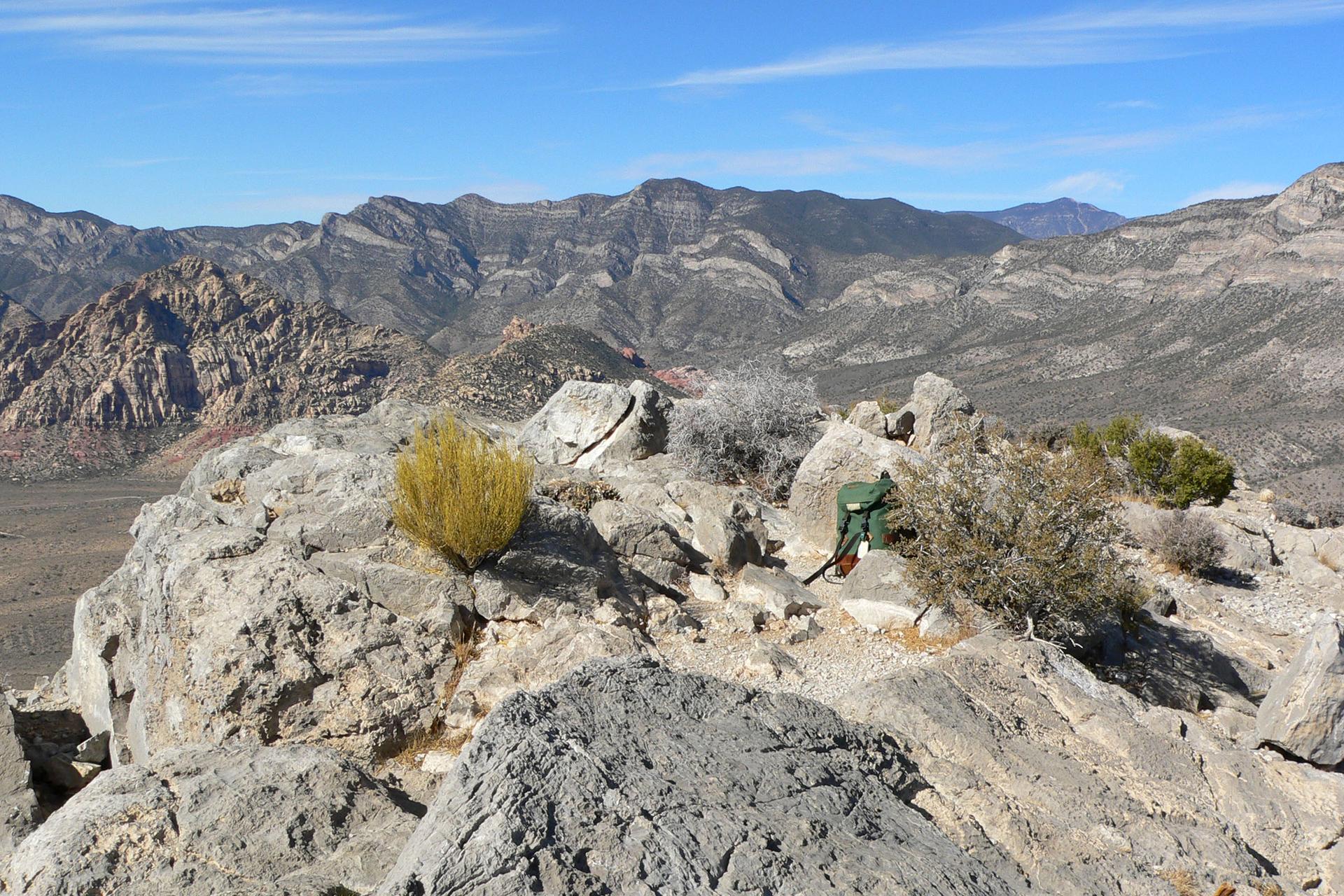 Green backpack on rocky outcrop overlooking a vast desert landscape.