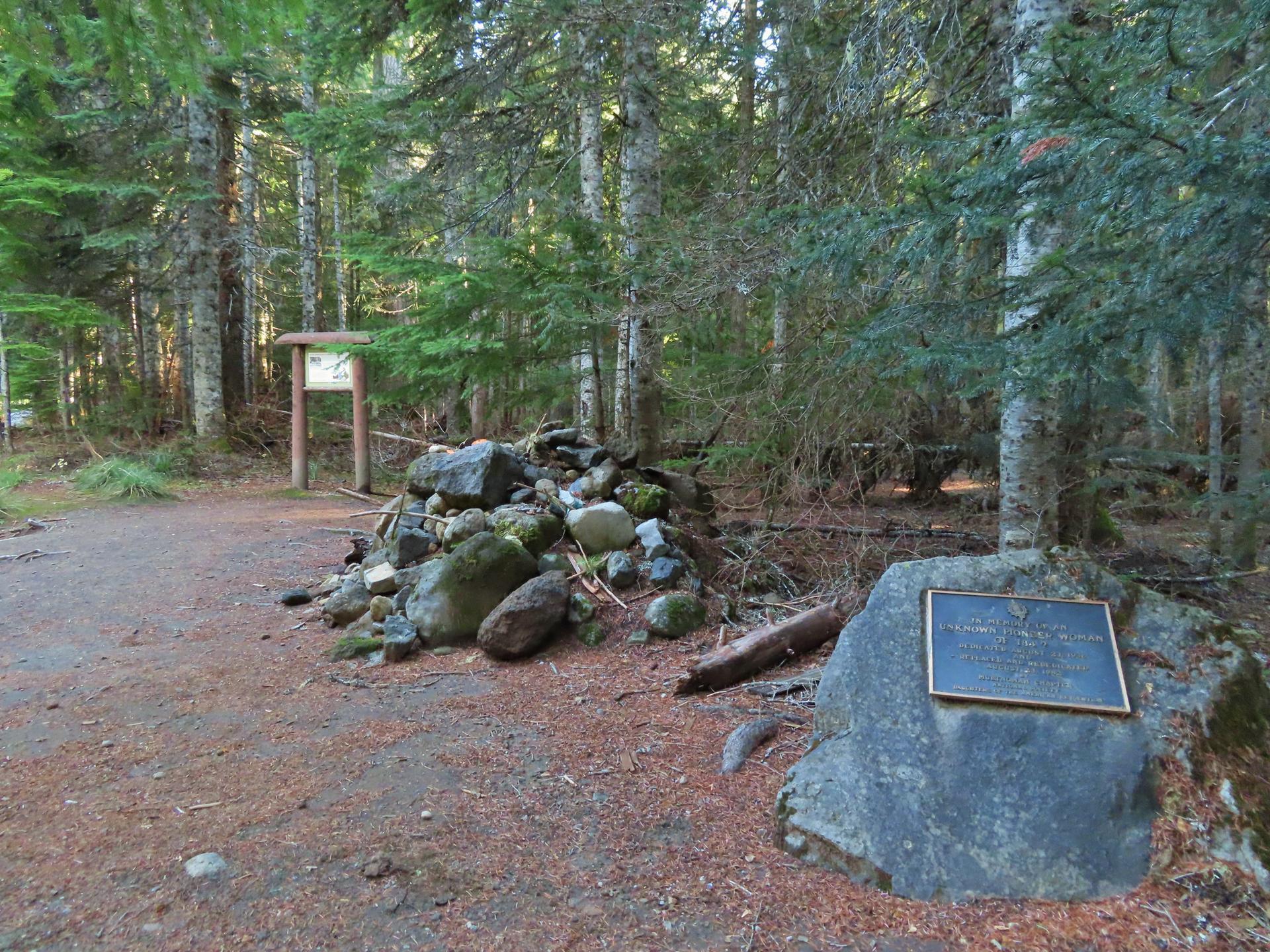 A forest path with a rock cairn and a plaque on a boulder in dappled light.
