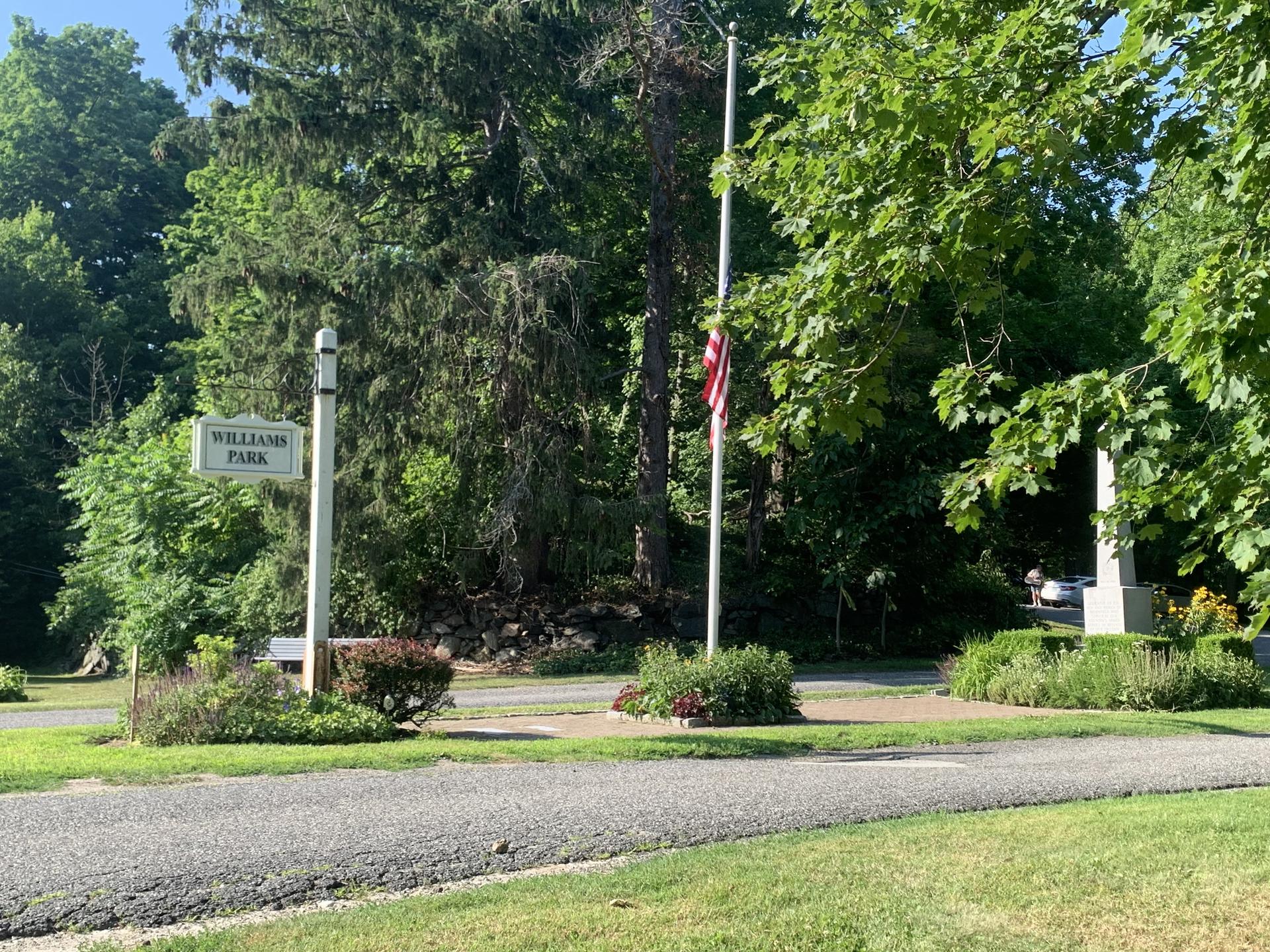 A park entrance sign, flagpole with flag, and monument on a sunny day.