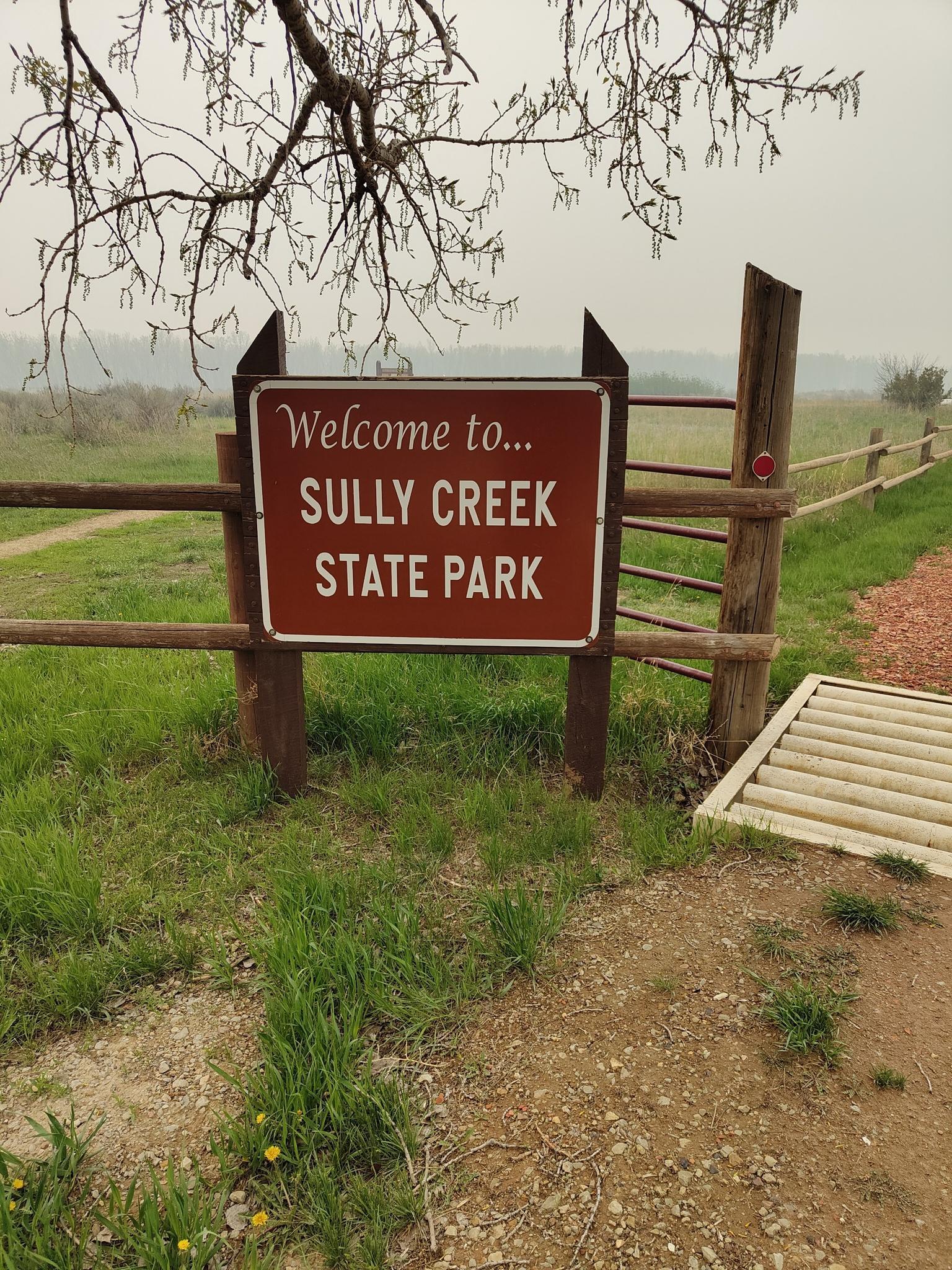 A 'Welcome to...' sign on a wooden fence in a hazy, grassy landscape.