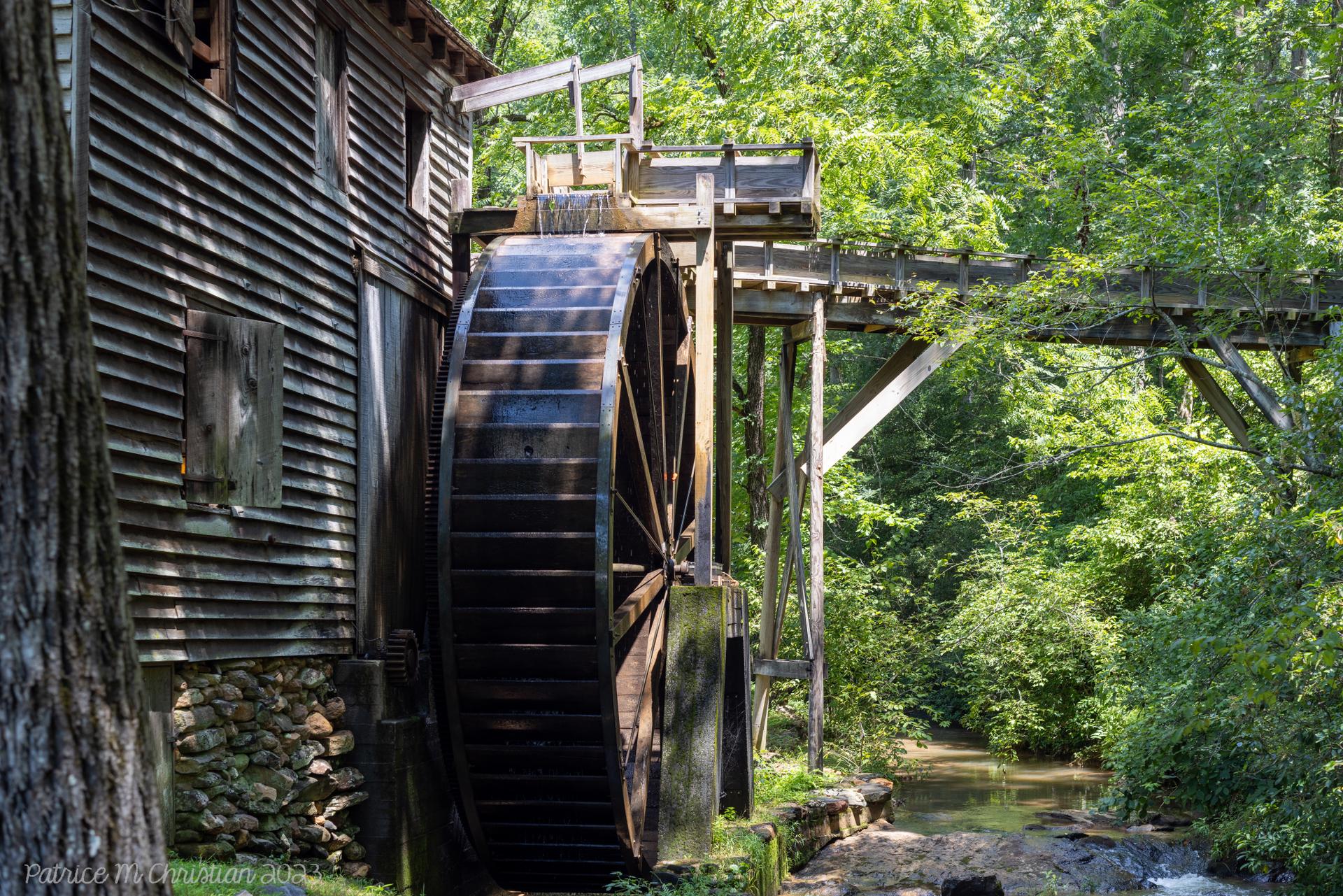 An old wooden water mill with a large wheel in a lush green forest.