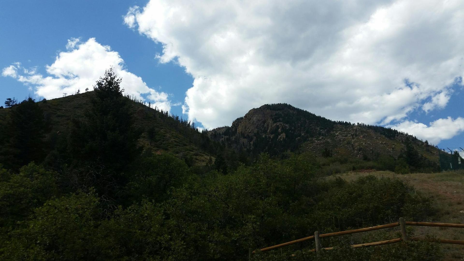 Lush green hills covered in trees under a partly cloudy blue sky.