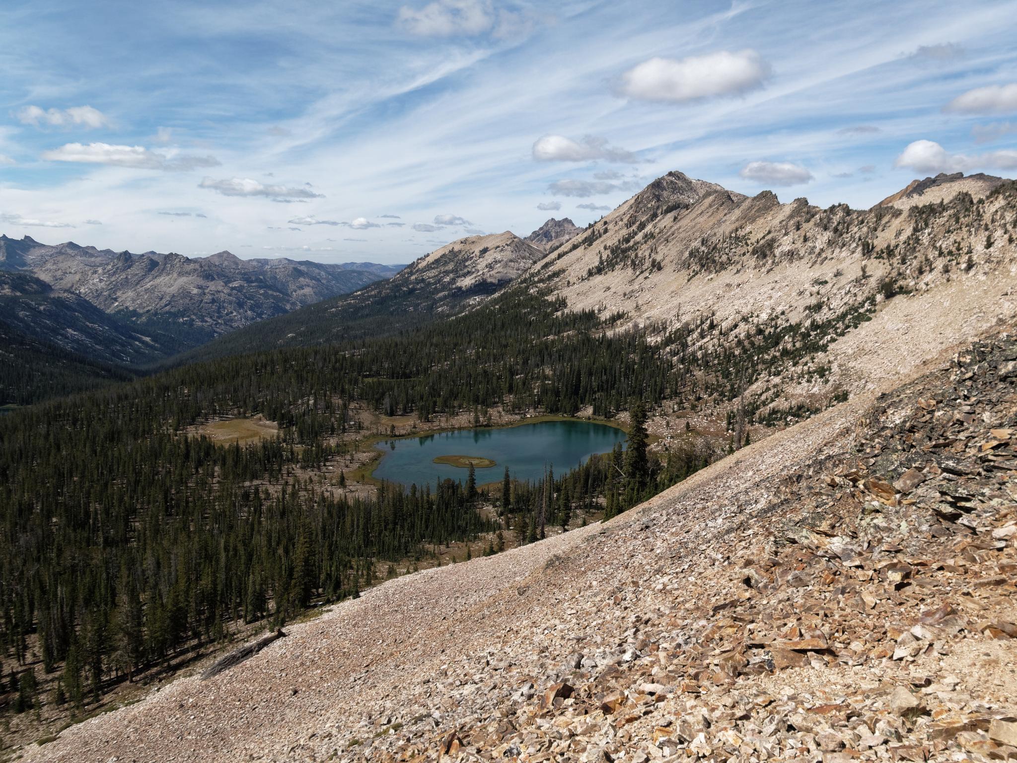 Panoramic view of a mountain lake nestled in a forested valley under a cloudy sky.