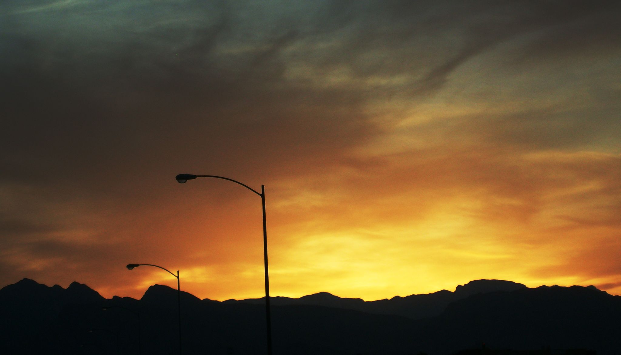 Silhouetted mountains and streetlights against a vibrant orange and yellow sunset sky. - Cheyenne Mountain